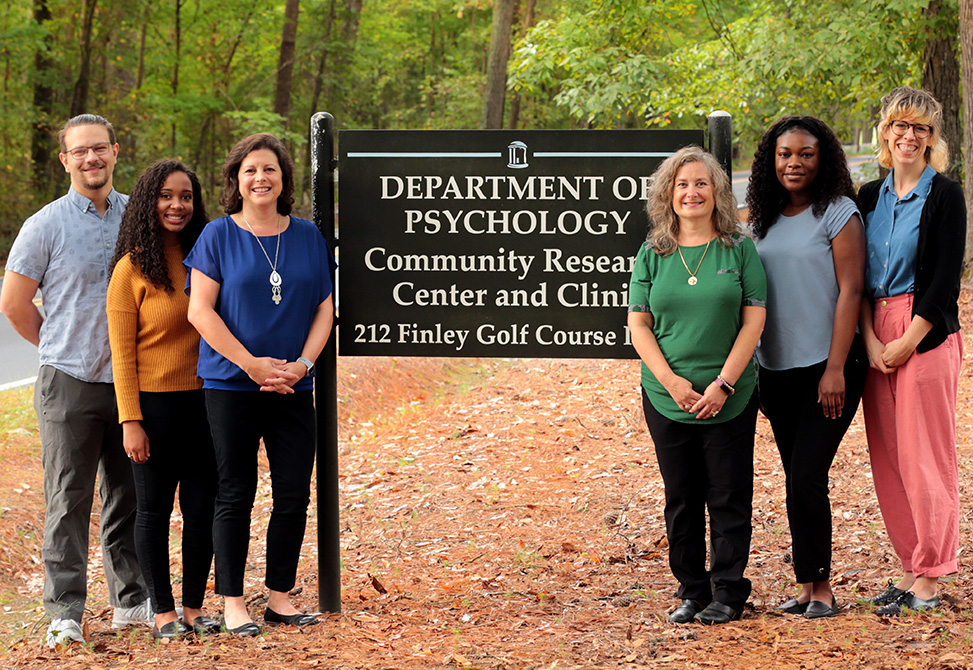 Clinic staff stands in front of the Department of Psychology sign
